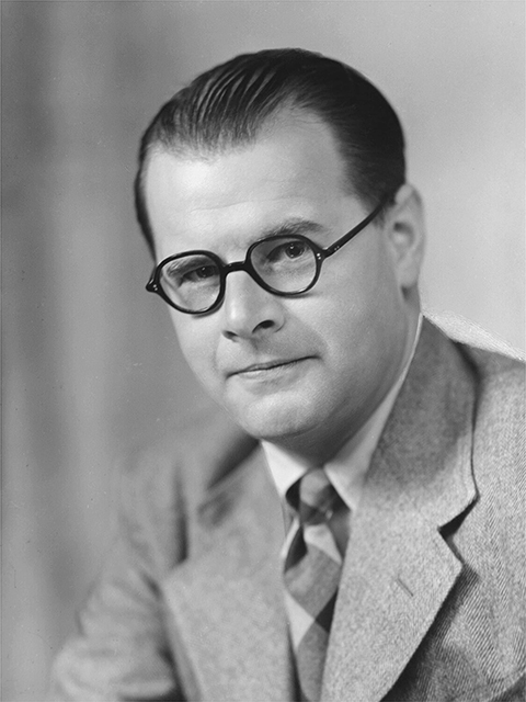 A man wearing a suit and dark-rimmed glasses poses for a closeup photograph.
