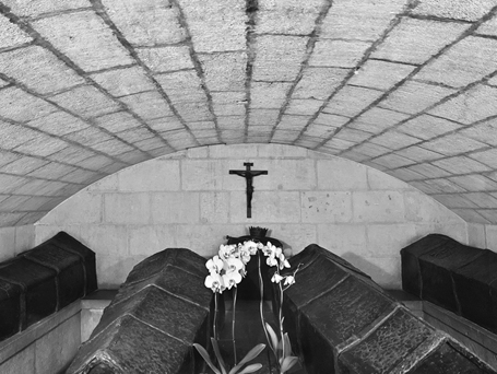 An undecorated arched stone chamber with five plainly decorated gilded wooden coffins arrayed before a small altar and plain crucifix on the back wall.