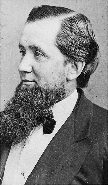 A man with a long dark-colored beard sitting for a formal portrait.