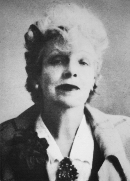 Figure 15. Anderson faces confidently forward with her head slightly tilted back and to the left. Her expression is neutral, with just the hint of a smile. She wears a jacket with a large, floral decoration on her lapel and a collared shirt closed at the collar with a glimmering brooch.