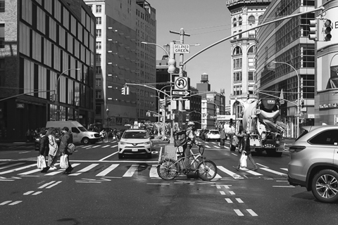 Figure 25. A city street is crowded with cars, trucks, taxis, pedestrians, and a food delivery worker on a bicycle.