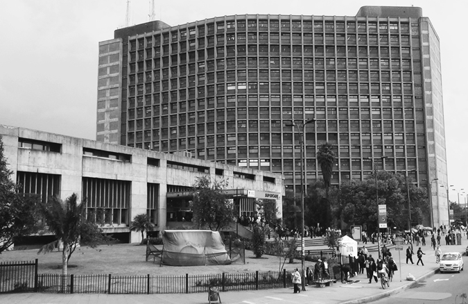 Figure 5.1A. A large city building stands in the background, with a smaller building in front of it at the left and a plaza in front of the smaller building.