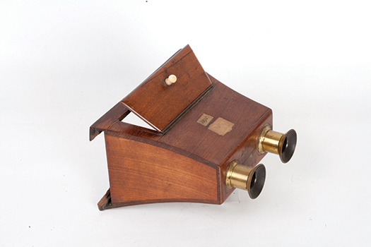 Figure I.2. A mahogany wooden box, seen from the side, with an open back where the stereograph is inserted. Two brass lenses protrude from the other side. On top, a small wooden door is open to let light in.