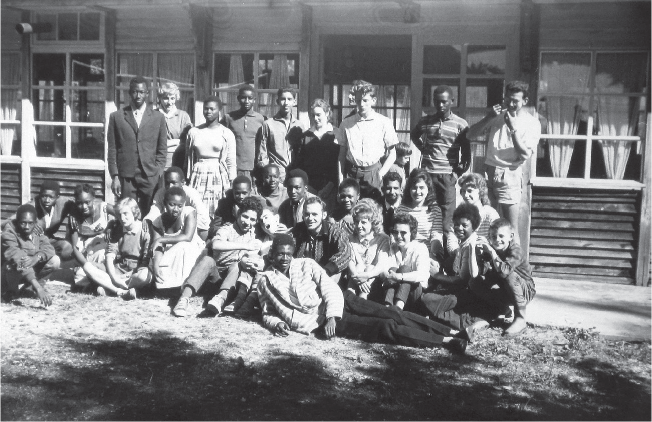 Students in a Franco-African exchange program sit and stand together in front of a cabin in the French Alps in 1960.