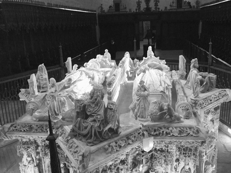 A lavishly decorated gothic-style star-shaped tomb with a royal couple lying in repose on top, surrounded by smaller upright figures in positions of prayer and various scenes carved in high relief on the sides.