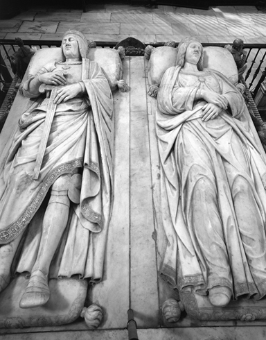 Two carved stone aristocratic figures lying in repose. The male figure on the left holds a sword, and the female figure on the right has clasped hands.