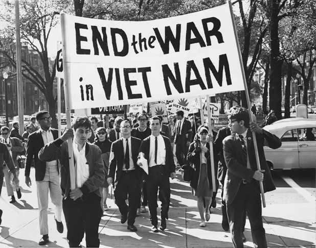 Figure 6. A group of young people march down the middle of a broad avenue. At the front two young men carry a sign that says “End the War in Vietnam.” Everyone is nicely dressed, most of the men with jackets and ties, the women with skirts and sweaters.