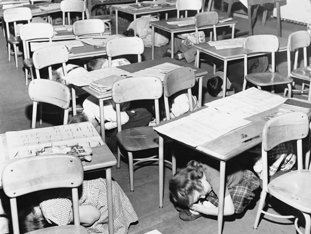 Figure 1. Young students are beneath their desks, on their knees, heads down in what was known as drop, duck and cover drills.