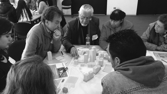 Figure 6.4. Several people sit at a table pointing at architectural models and buildings.