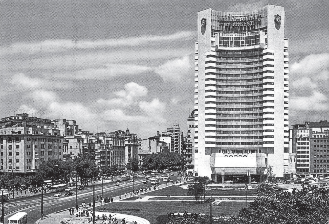 A tall white building in the middle of Bucharest towers above smaller buildings across the road. There are trees and sidewalks on either side of the road, and in front of the hotel is a park with walkways.