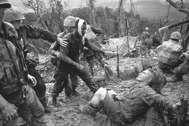 Figure 9. In a first aid center for wounded American soldiers, one soldier reaches out for a badly wounded GI walking into the center with his head bandaged, heading toward another wounded man, sprawled in the mud with his pants leg cut away and his kneed bandaged.