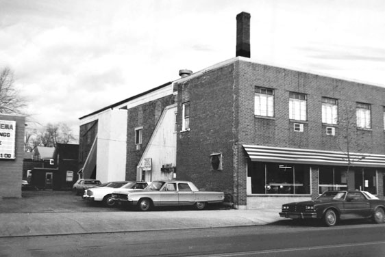 Figure 16 A tiny parking lot sits between a small movie theater and a run-down-looking brick building housing a laundromat. The theater marquee is barely visible at far left.