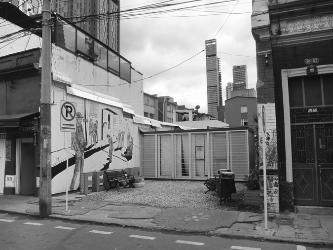 Figure 6.5. An empty lot with benches on a city street, surrounded by buildings. A shipping container spans the width of the back part of the lot.