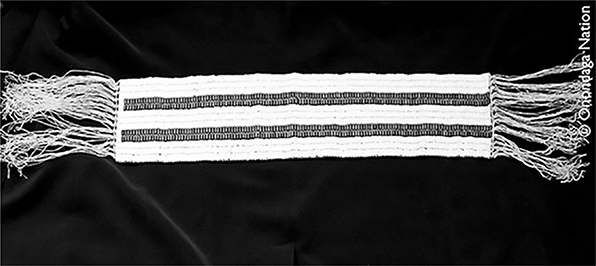 White shell bead wampum belt with three rows of white beads along the top. In the middle are two rows of purple beads, three more rows of white beads, and two more rows of purple beads. The bottom contains three final rows of white beads.