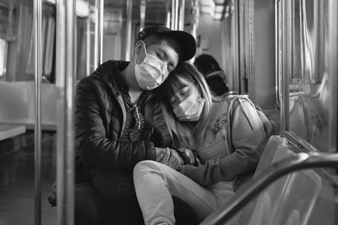 Figure 13. In a subway car on a Queens-bound R train, a young, masked couple with their eyes closed are slumped in each other’s arms.