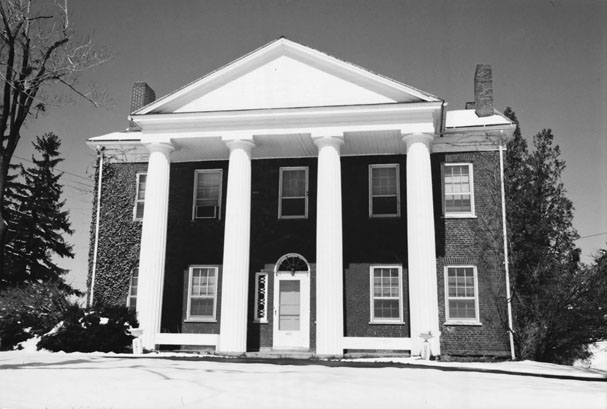 Figure 5 A large two-story brick house with a chimney at either end has five evenly spaced windows over four similar windows and a central door. An imposing two-story white-painted portico with four massive columns extends almost the width of the house.