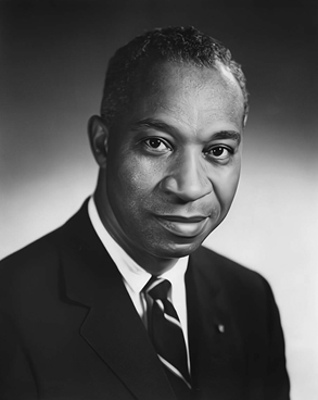 A formal portrait of a man wearing a dark suit with a striped tie. The man is looking directly at the camera and smiling slightly.