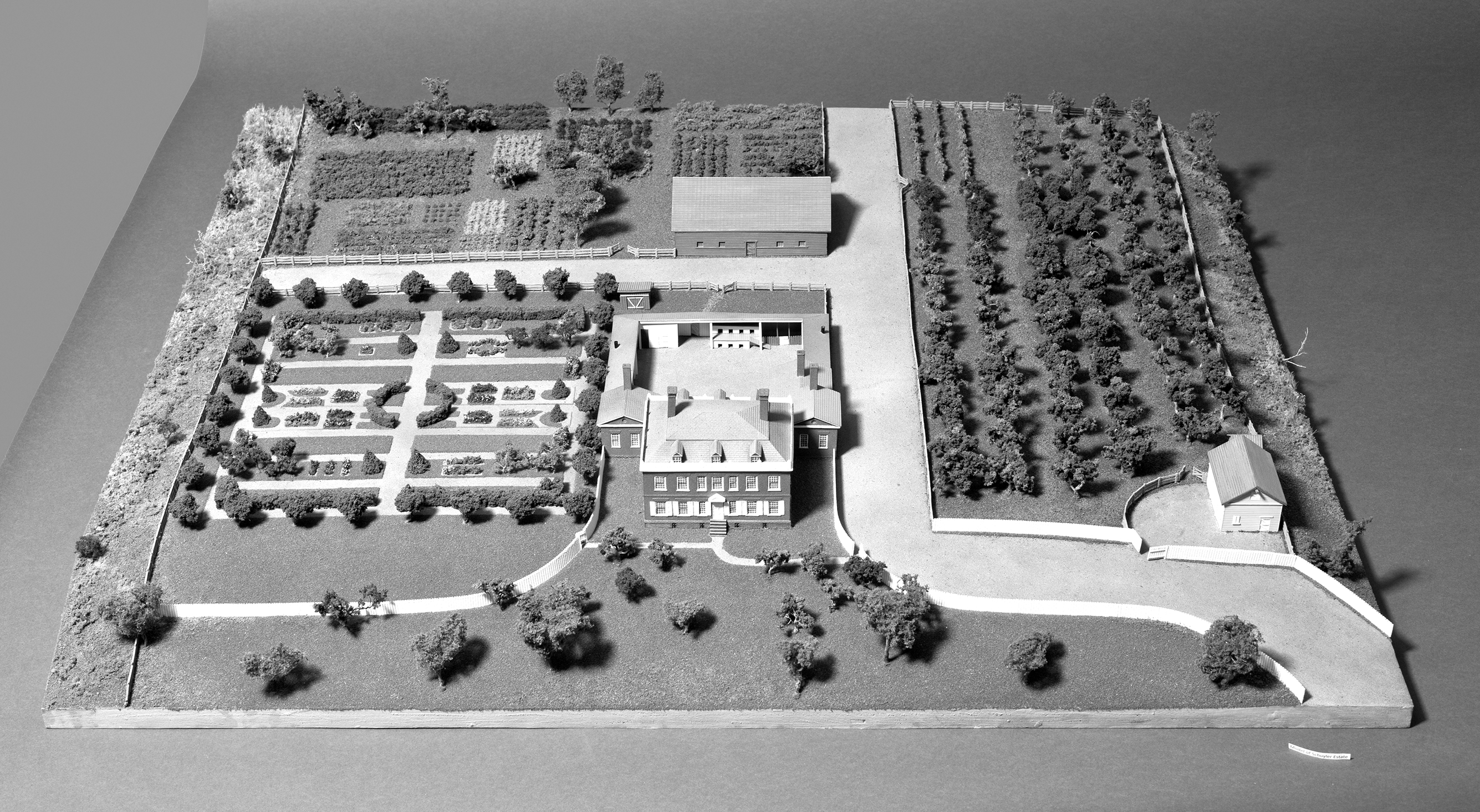 A model shows the Schuyler mansion with enclosed work area in the back, gardens, road to the home, path to the front entrance, barn, and a small building that likely served as a stable.