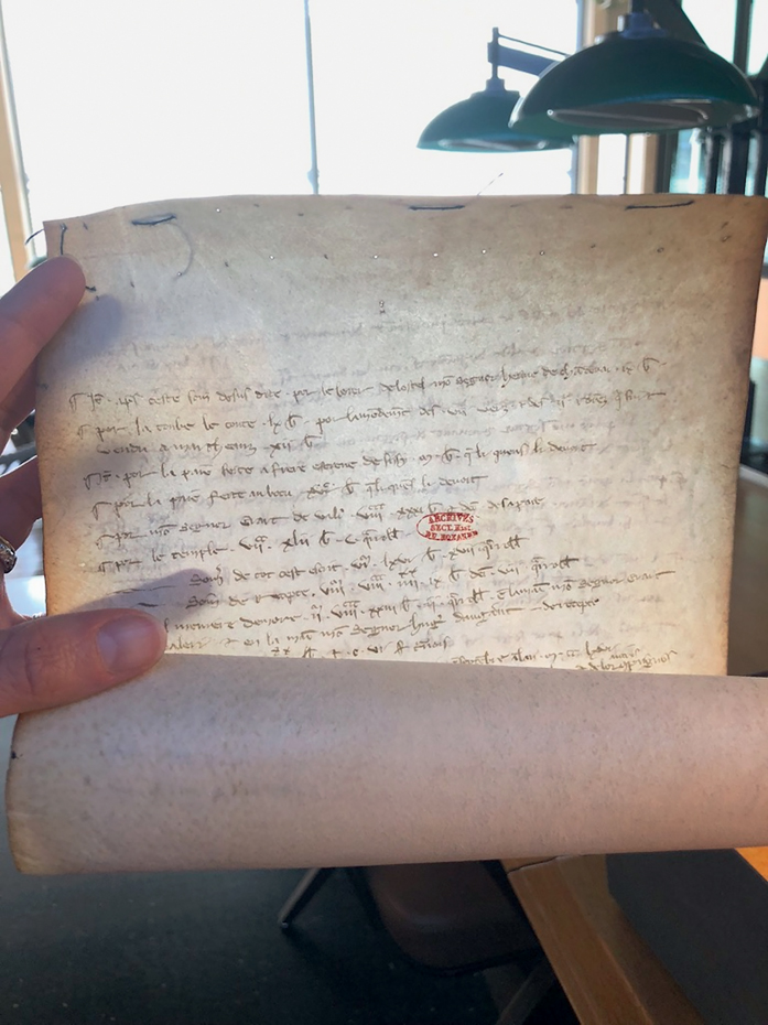 Figure 6. A medieval parchment roll, opened and held up to the light by a hand to expose stiches at the top of the document.