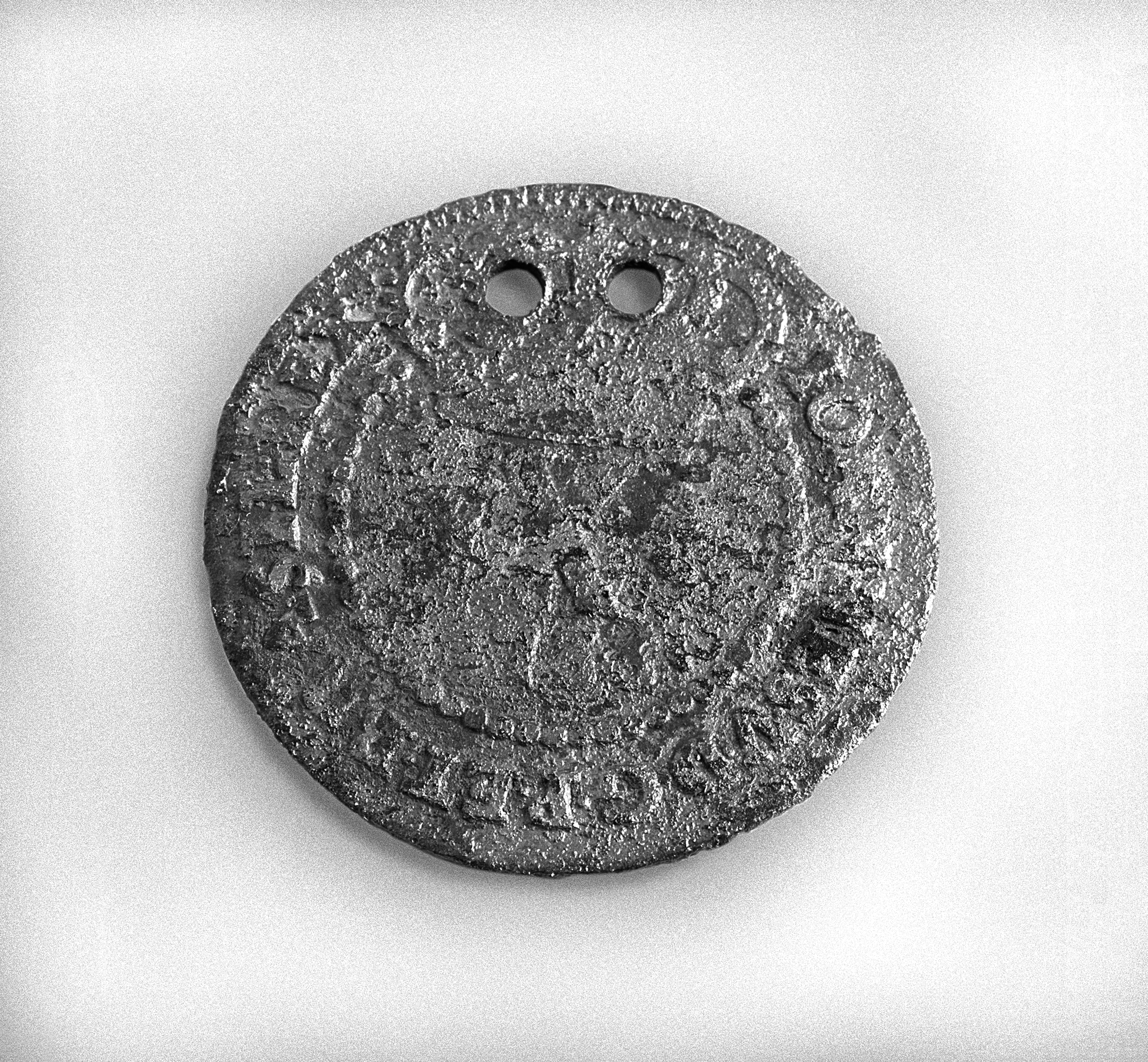 An old copper alloy coin with two holes pierced on one side. An X is visible in the center of the coin.