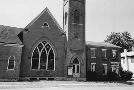 Figure 4 A simple two-story brick house appears to be attached to a much larger brick church with pointed-arch windows and doors. The house has three windows on its second floor, above two similar windows and a door framed by pairs of inset columns on the ground floor. The church tower, virtually adjoining the house, is twice the height of the house.
