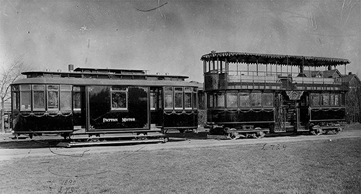 An experimental electric railroad passenger car, with “Patton Motor” written on its side, and a two-level railroad streetcar, end to end on rail tracks. Grass appears in the foreground.