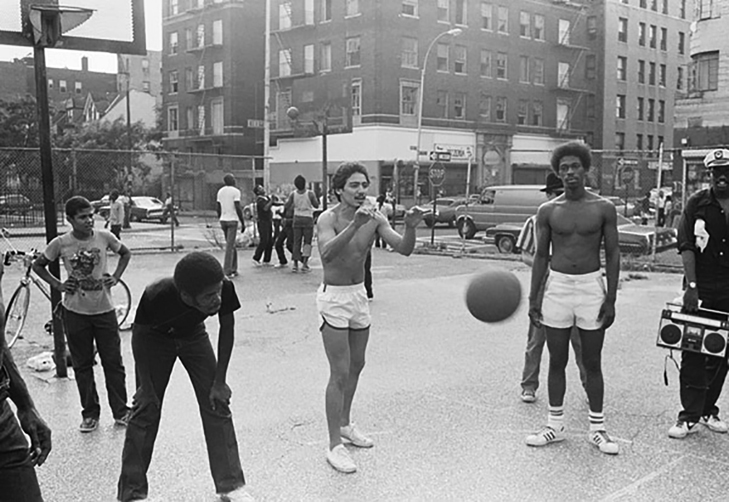 Cold Crush Brothers on an outdoor court, with Fab 5 Freddy holding a boom box. Another game—and traffic on the street—appear in the background.
