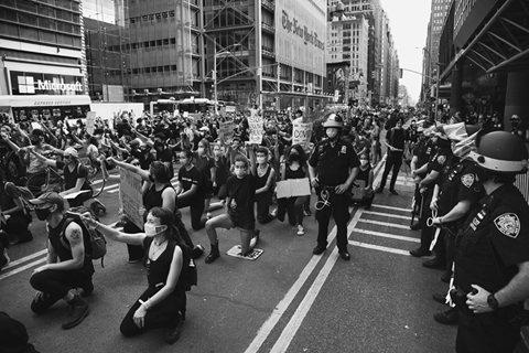 Figure 16. Black Lives Matter demonstrators on their knees with fists raised are flanked by police in midtown Manhattan.