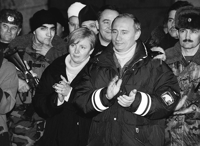 Vladimir Putin and his wife Liudmila in Chechnya, standing and clapping with Russian soldiers standing behind them, January 2000.