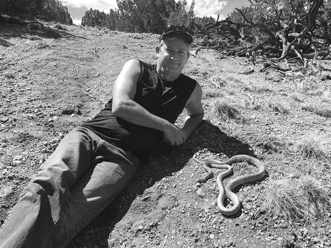 Robert Lovich reclines on the ground next to a Coachwhip snake.