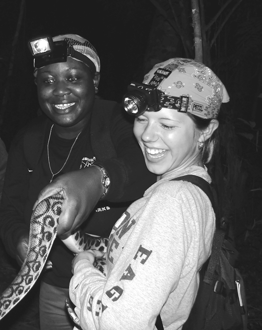 Two students in a tropical ecology class in Peru, smiling and laughing, hold a Rainbow Boa.