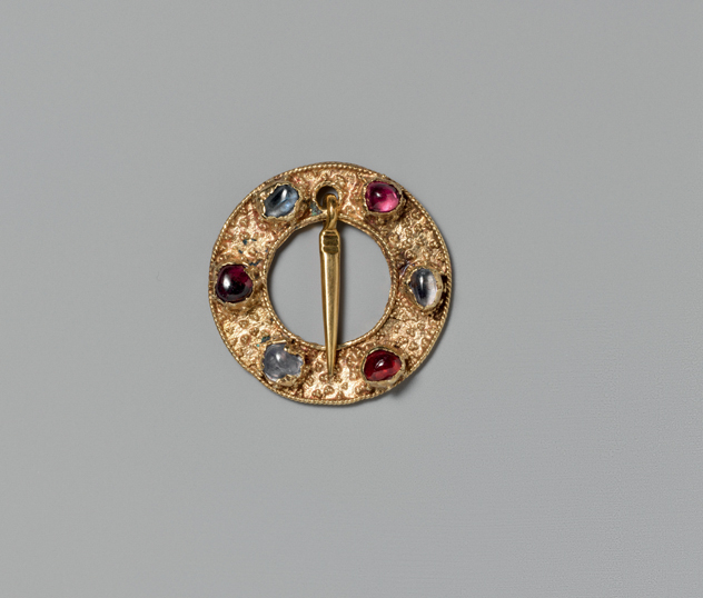 Figure 18. A gold, donut-shaped brooch with six multicolored mounted gems and a small gold pendant.