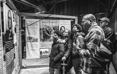 Five people are reading the information on a large poster display at the Dreaming of Timbuctoo exhibition.
