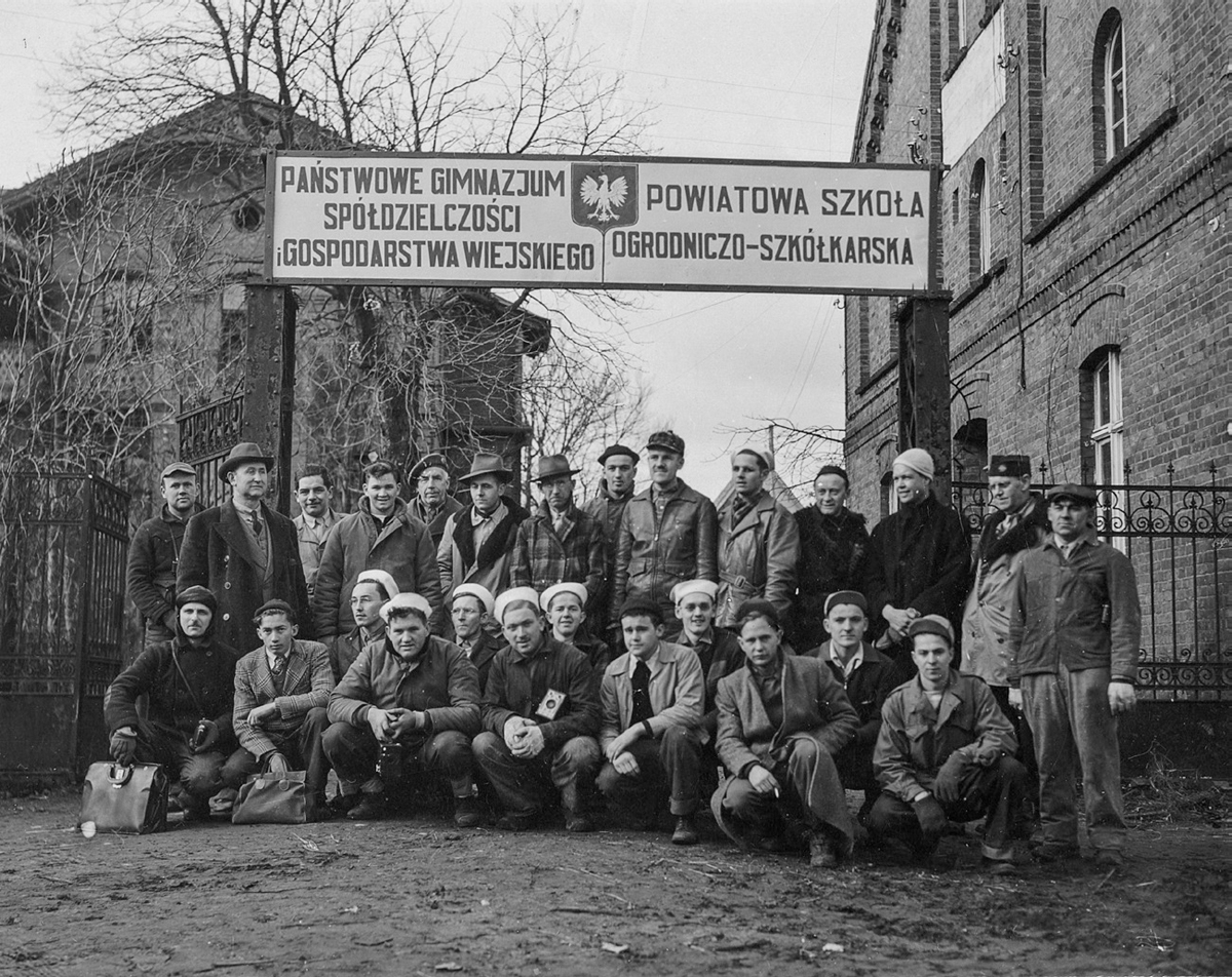 Figure 15. A group of men stand under a sign with Polish writing on it.