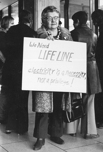 Figure 53. An older woman stands with a handwritten sign saying, “We need Lifeline, electricity is a necessity, not a privilege!”