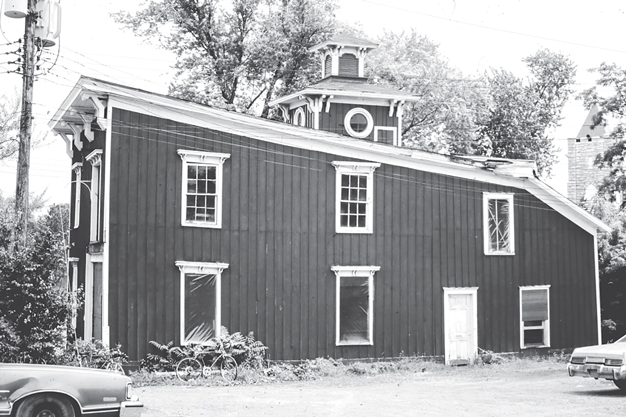 Figure 7. A two-story board-and-batten barn has a flat roof sloped front to back with an elegant cupola. Some of the window sashes have been replaced by plastic sheeting.