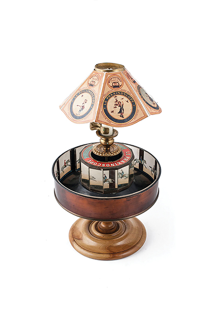 Figure 5.8. A device composed of a brass drum, a strip of sequential images placed around the inner edge of the drum, mirrored panels at the center, and a lamp. A lampshade over the device is illustrated with pictures of children playing.