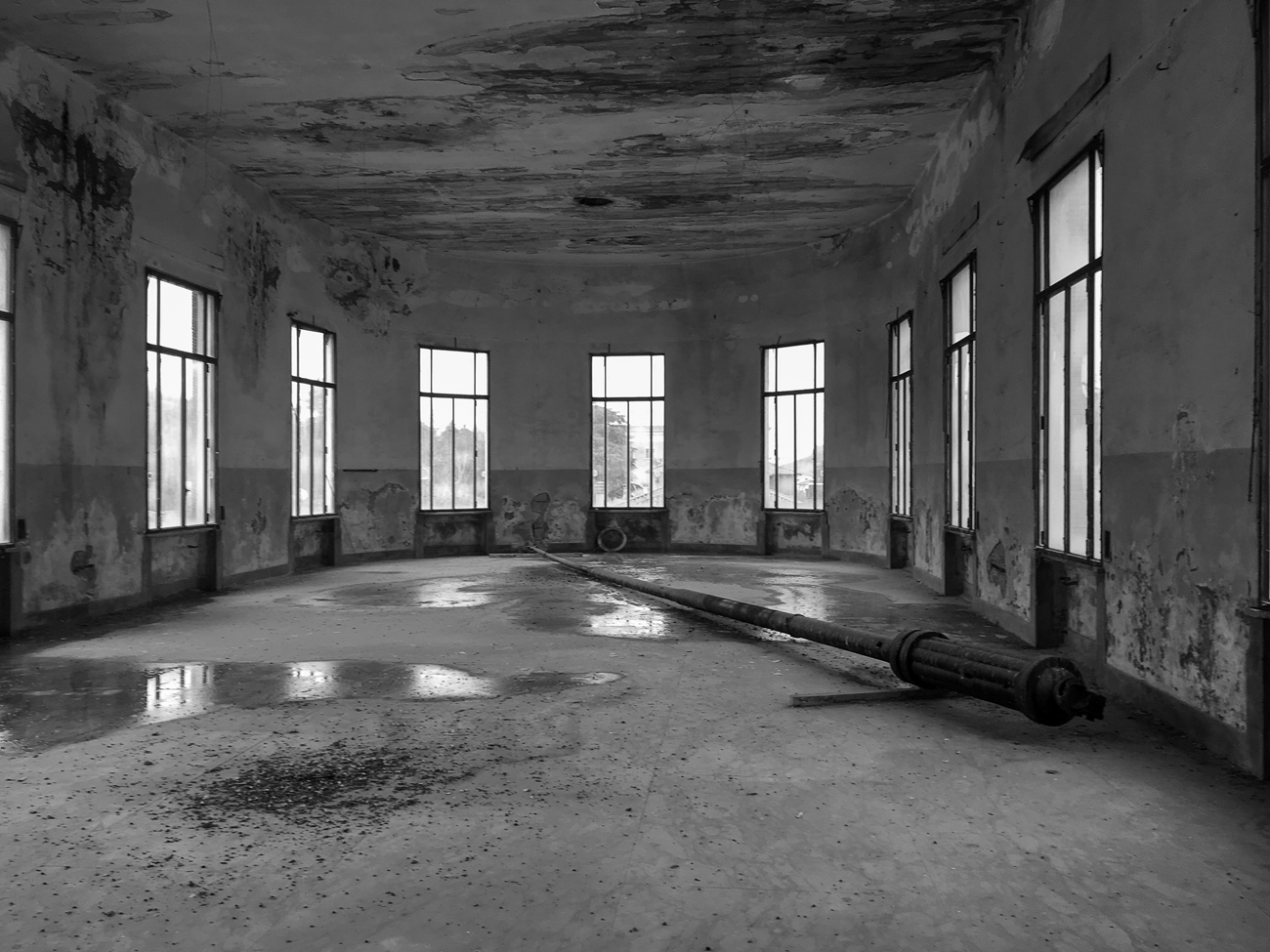 Figure 4.6. A large empty room filled with puddles and stains, dotted by tall windows. A long iron flagpole lies abandoned in the middle of it.