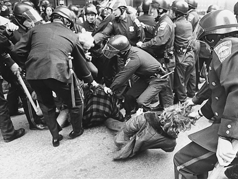 Figure 47. A scrum of helmeted police arrest two protestors sitting on the ground. Two policemen are dragging one protestor away by his hair. Three other police are pulling on the jacket of the other.