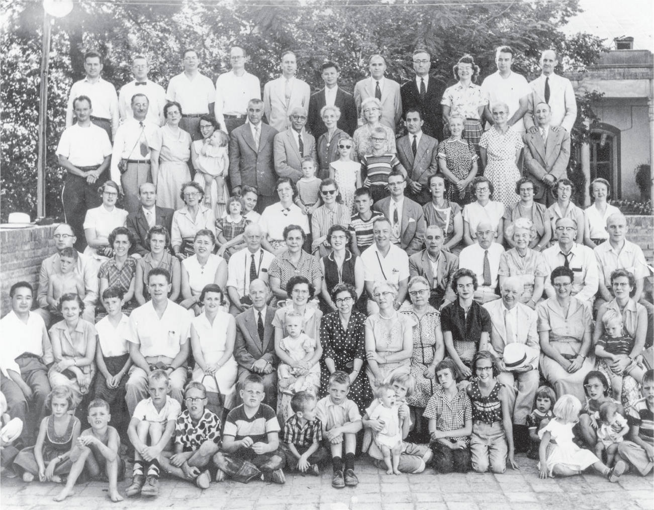 A black-and-white photograph of the Presbyterian missionaries who were in Tehran in summer 1957. Dozens of individuals are sitting and/or standing in six rows, with missionary children in the front. The image conveys the homogenous demographics and tight-knit nature of the Del Be Del network.