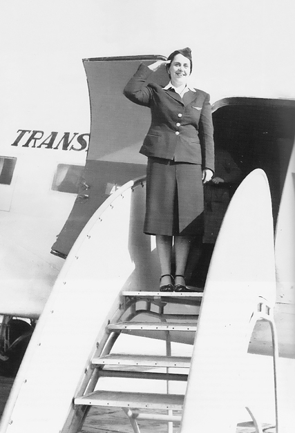 Figure 5.1. A woman in a dark blazer raises her hand to her head in a salute with a smile, standing at the top of the boarding stairs of a JAT DC-3 plane.