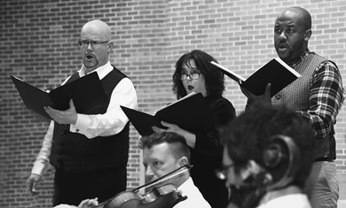 Three soloists from the Northern Lights Choir of Saranac Lake, with string musicians accompanying them in the foreground, perform Promised Land: An Adirondack Folk Opera.