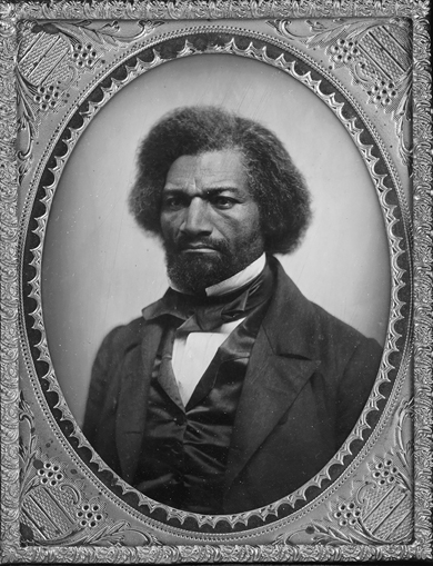 A formal headshot of Frederick Douglass against a black backdrop. A scowl fixes his wide mouth, and his brow is drawn over stern, unsmiling eyes. His coat is well-fitted, his gleaming vest and tie match well, and his white collar frames his chin as tightly as the oval frame sets off the portrait.