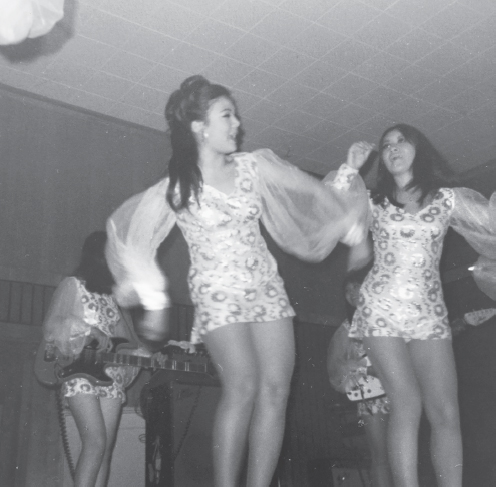 Two female Vietnamese dancers and a female band performing at a noncommissioned officers’ club. The dancer in the foreground has a 1960s bouffant hairstyle. All of the women are in minidresses