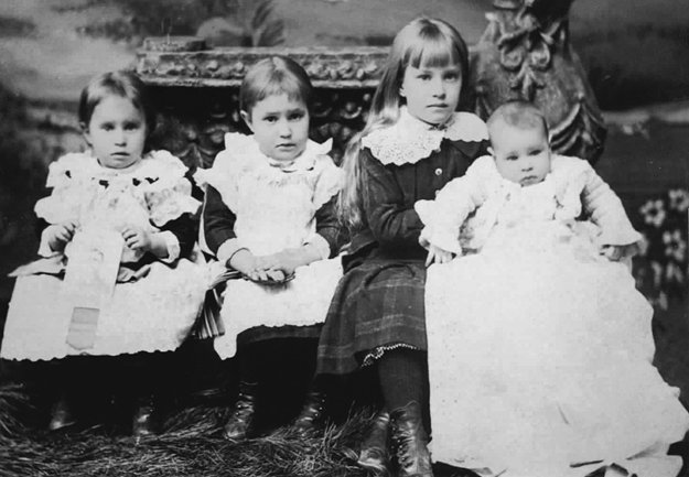 Figure 4. Three children and an infant, formally dressed and showing little expression. The child on the left holds a photograph, the next has her hands folded in her lap, and the third holds the infant up on her right knee.