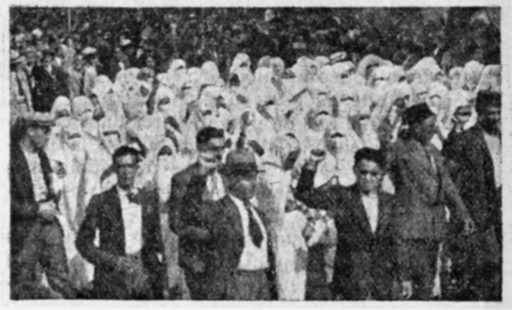 Figure 2.4. A black-and-white photograph of Muslim women dressed in white haiks in a group behind men in a protest