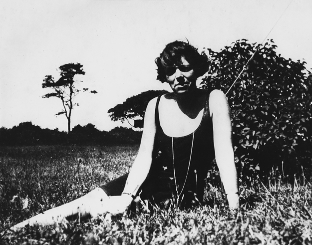 Figure 9. Anderson lounges in the grass, wearing a one-piece bathing suit. She has a hint of a smile, and her hair blows gently in the wind. Her legs are outstretched to the left and she props herself up on her right arm while her left arm rests in front of her.