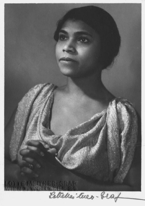 A young Black woman in a shimmery top clasps her hands in prayer.