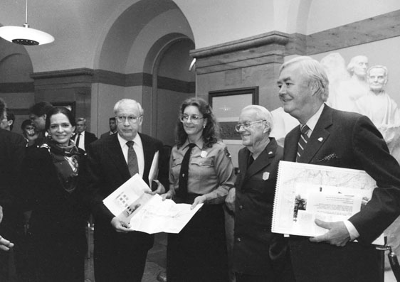 Figure 17 Two women and three men pose for a group photo in front of a partly visible marble statuary group. The woman and man in the center are in park ranger uniforms.