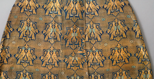 Figure 19.3. A repeating pattern of paired hunting birds and star-shaped designs woven into a gold and dark blue colored fabric.